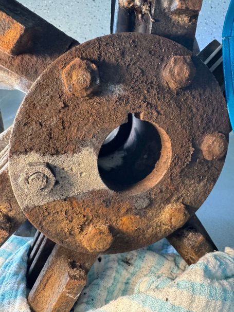 Rostige Metallkupplung mit Schrauben und einer runden Öffnung in der Mitte.