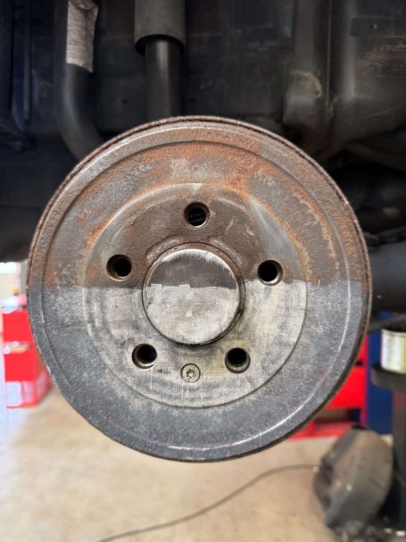 Bremsscheibe mit Rostflecken und mehreren Bohrungen, unter einem Fahrzeug montiert.
